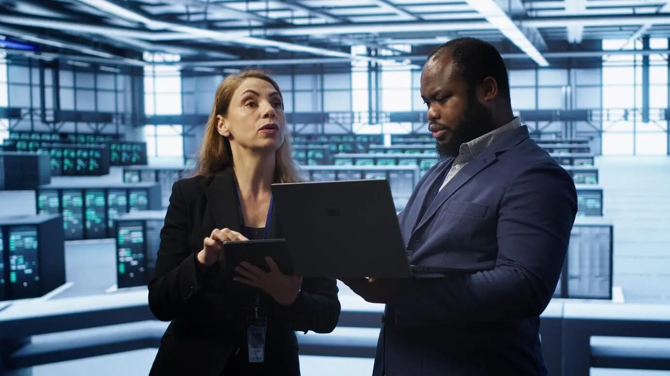 Руководитель на серверной ферме контролирует работу инженера, устраняющего сетевые неполадки.